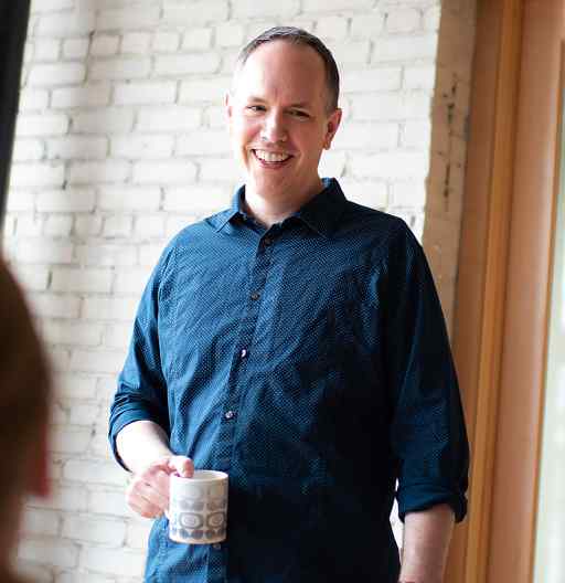 Dan at the office, standing and talking to a group while holding coffee mug